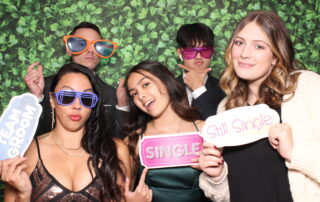 Guests posing with fun props in front of a hedge wall backdrop, captured from the open-air photo booth at an event in Metro Detroit.