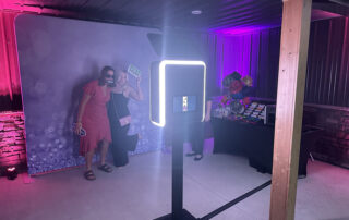 Guests pose with props in front of a modern open-air photo booth with a purple backdrop at a Metro Detroit celebration.